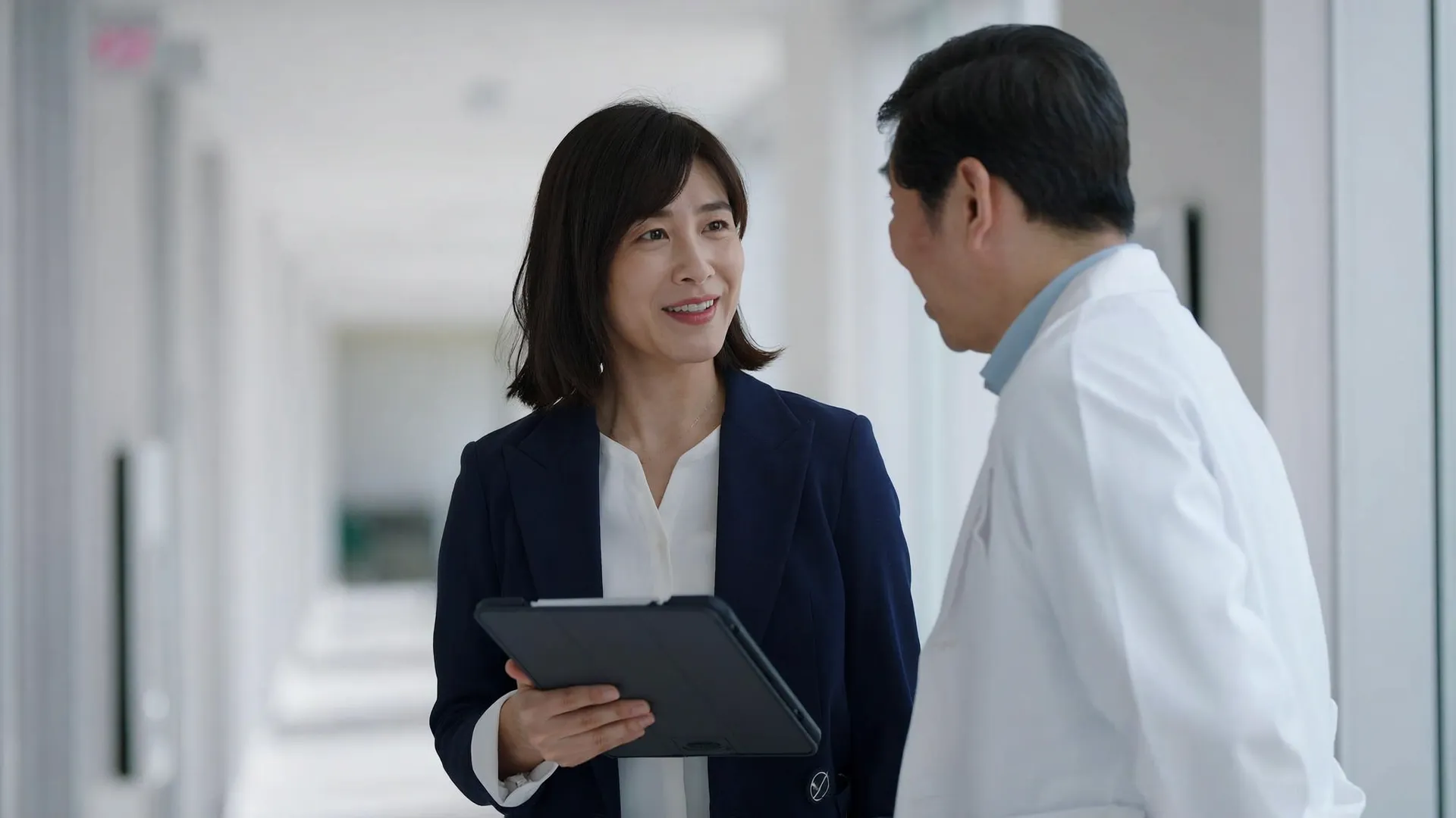 A sales representative and a physician talking in a clinic hallway over a tablet
